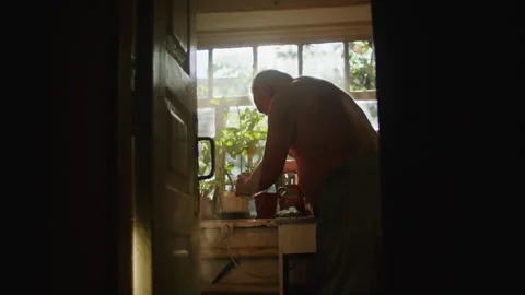 Older man standing by a window preparing food. Natural light from windows in the Stock Footage 276887930