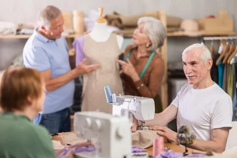 Older man stitching at machine during sewing class for seniors Stock Photos