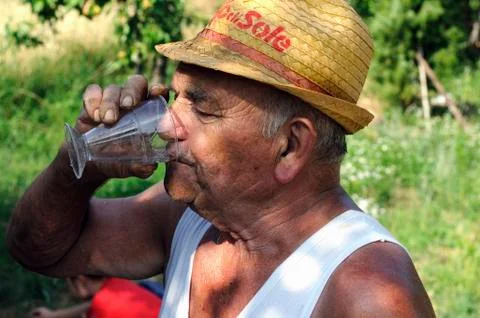 An older man in a straw hat drinking a glass of white wine Stock Photos