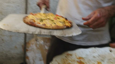 An older man talks to the camera and removes a pizza from a brick oven Video stock 62862843