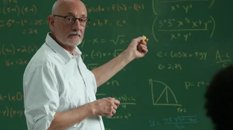 Older man teaching in classroom pointing at diagrams on a blackboard Stock Footage