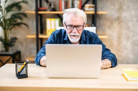 Older man is using laptop for working indoor Stock Photos