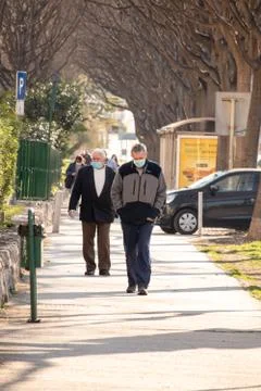 Older man walking down a street in Split wearing a medical face mask , anothe Stock Photos