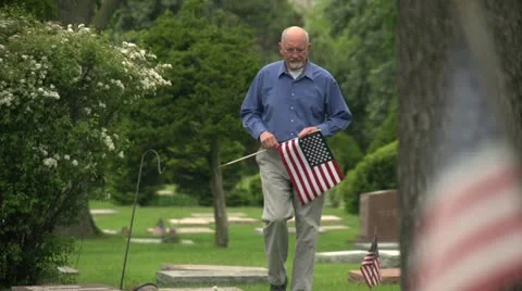 Older man walking through cemetery holding US flag Vidéo 10972663
