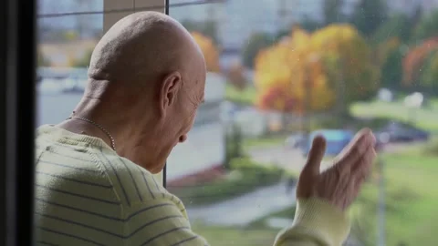 Older man waving with hand through window glass to family or friends Video stock 218387655