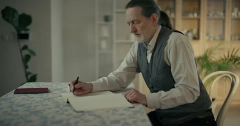 Older man writing notes in a notebook at a dining table Stock Footage 336276437