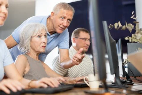 Older mentor explaining something to elderly woman during computer class Stock Photos