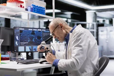 Older researcher uses microscope as observation tool with tray of samples Stock Photos