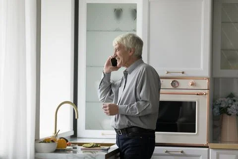 Older single man talking on smartphone standing in kitchen Stock Photos