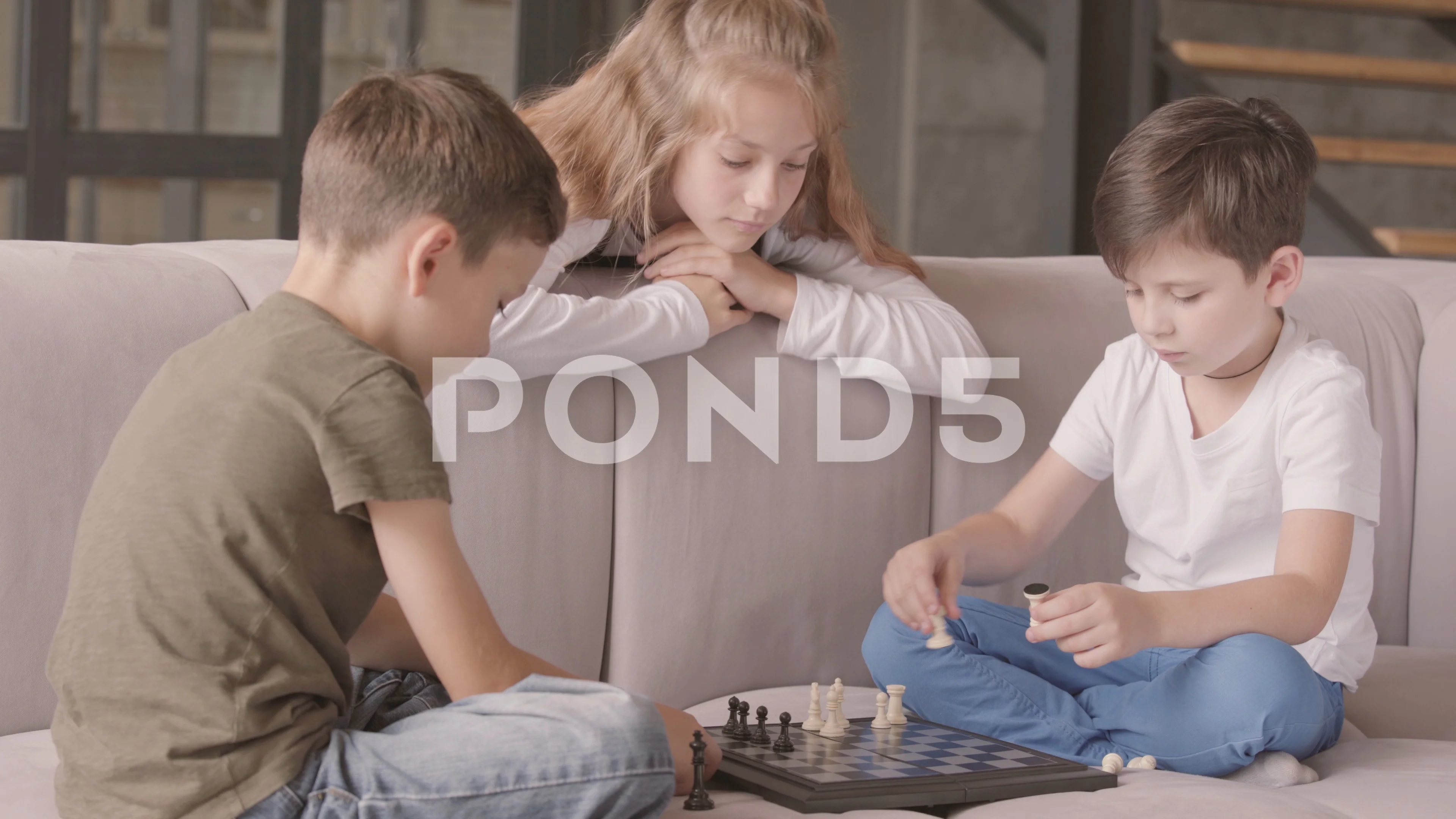 Older sister and two younger brothers playing chess sitting on the couch at  home