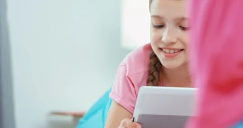 Older sisters using tablet pc, lying on the bed and younger sister playing near Stock Footage 95621890