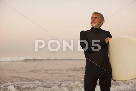Older Surfer Carrying Board On Beach