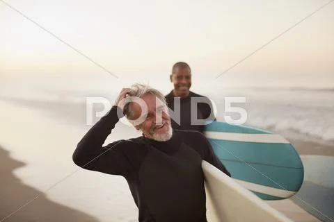 Older surfers carrying boards on beach Stock Photos