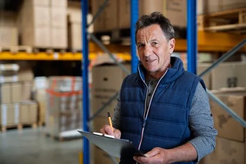 Older warehouse worker working looking at document in clipboard. Stock Photos