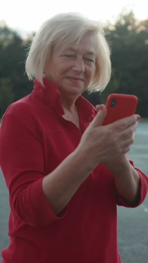 An Older Woman Engaged in Using Her Smartphone While in a Bright Outdoor Setting Stock Footage 301825911