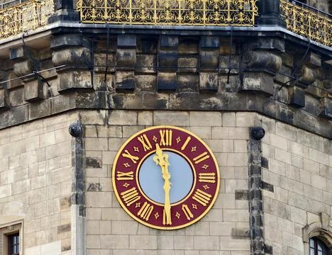 Oldfashioned stone clock tower with vivid red face and ornate gilded hands .. Stock Photos