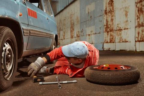 Oldtimer car enthusiast in overall replacing car wheel Stock Photos