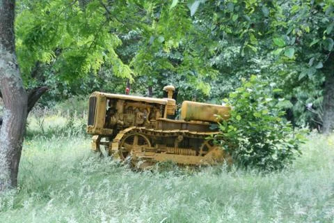 Oldtimer caterpillar tractor being overgrown in the field Stockfoto's