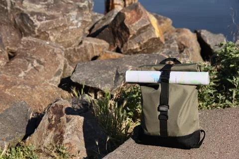 Olive green roll-top backpack with a rolled map attached, outdoor adventure a Stock Photos