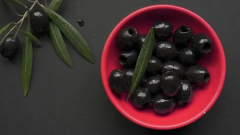 Olive leaf falling into scarlet bowl with black olives 4k 120fps Stock Footage 334941862