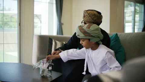 Omani father and son inserting money in money jar. Stock Footage 151268568