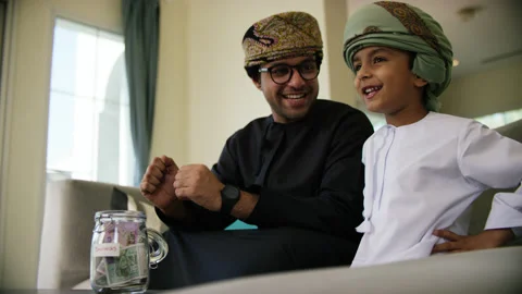 Omani father and son inserting money in money jar. Stock Footage 151269404