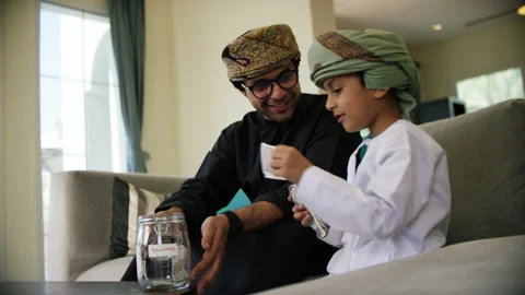 Omani father and son inserting money in money jar. Stock Footage 151272620