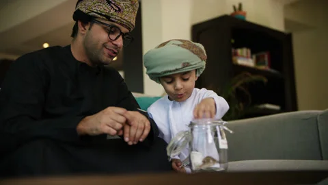 Omani father and son inserting money in money jar. Stock Footage 151273910