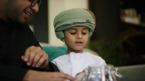 Omani father and son inserting money in money jar. Stock Footage 151274342