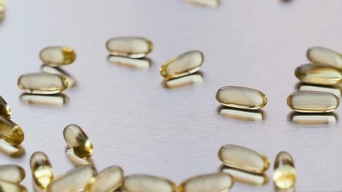Omega 3 capsules falling on a metal surface Stock Footage 72372076