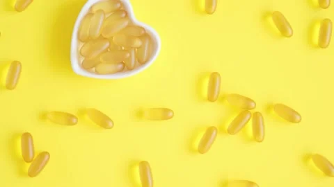 Omega 3 capsules in a heart-shaped plate on yellow background. Fish oil softgels Stock Footage 155133703