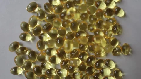 Omega 3 softgel capsules scattered across white surface in closeup Видео 342611255