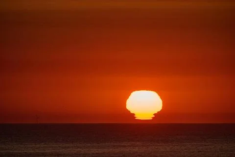 Omega sun setting over ocean horizon at dusk Stock Photos