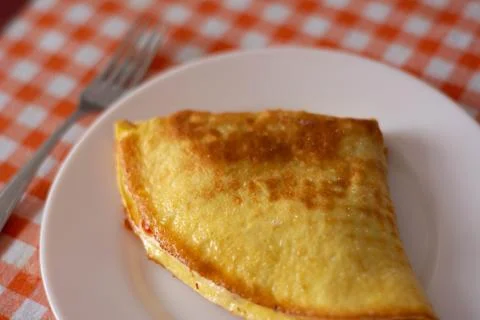 Omelet on white plate with fork on checkered tablecloth, cozy breakfast scene Stock Photos