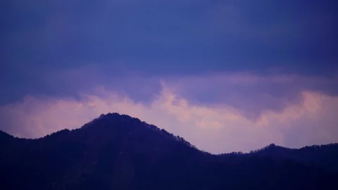 Ominous clouds gather and travel on silhouette of Mountains at dusk Stock Footage