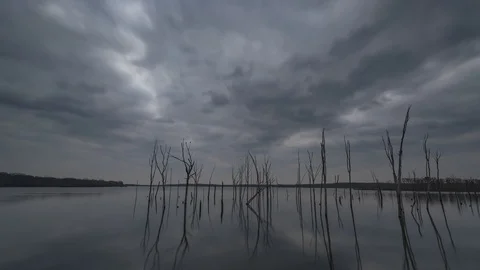 Ominous clouds swiftly passing over a still lake with trees in the water Stock Footage 101312289