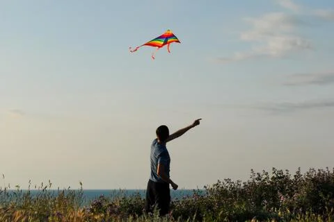 One active young man controls colorful kite floating in air at sunset near sea 스톡 사진