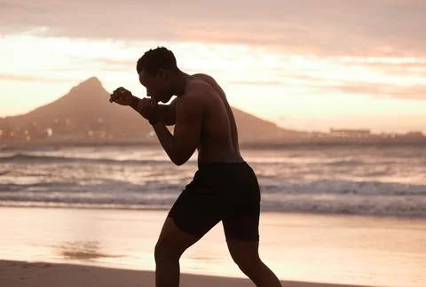 One african american man practicing shadow boxing on a beach at sunset. Black Stock Photos