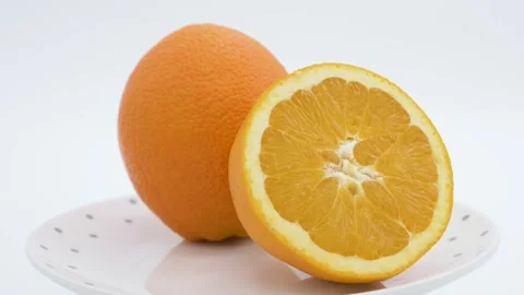 One and a half juicy oranges rotating on a plate with white background Stock Footage