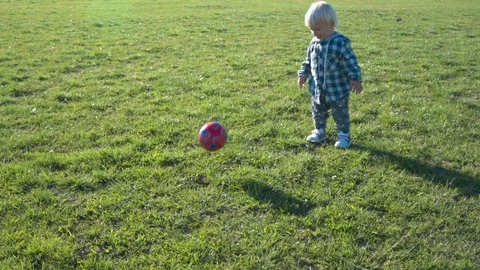 One and a half year old boy joyfully chases the ball on the field Stock Footage