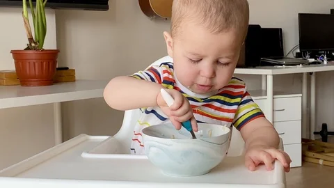 One and a half year old baby eating oatmeal himself. Happy kid eat porridge Stock Footage 129003651
