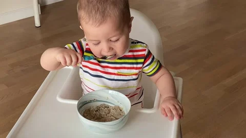 One and a half year old baby eating oatmeal himself. Happy kid eat porridge Видео 131821649