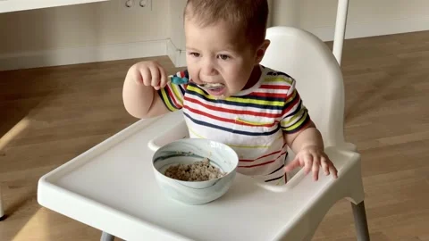 One and a half year old baby eating oatmeal himself. Happy kid eat porridge with Stock Footage 131821697