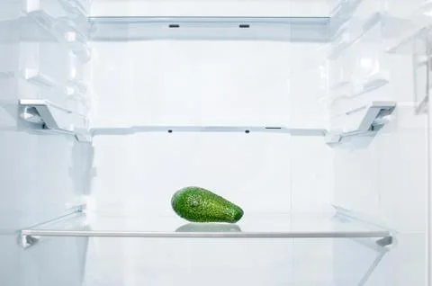 One avocado lies on a shelf in an empty refrigerator Stock Photos