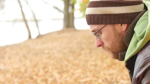 One bearded man lights a cigarette on a bench in autumn park. Thoughtful serious Vidéo 68970779