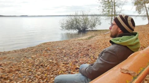 One bearded man lights a cigarette on a bench in autumn park. Thoughtful serious Vidéo 68970992