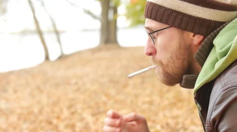 One bearded man lights a cigarette on a bench in autumn park. Thoughtful serious Stock Footage 68971392