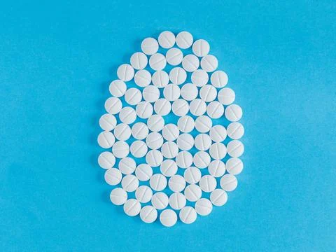 One big Easter egg made from medical pills on blue background. Stock Photos