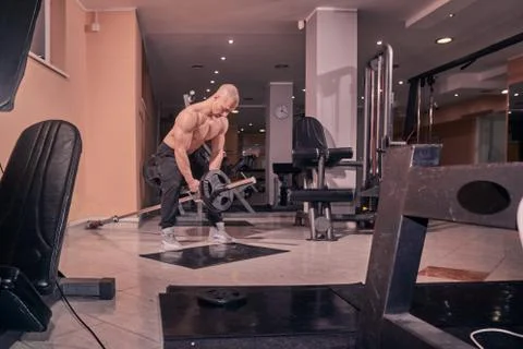 One bodybuilder, exercise T-bar row, gym interior, fitness equipment. Stock Photos