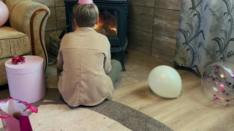 One boy sitting by the fireplace alone surrounded by balloons and gifts. Stock Footage 293617891